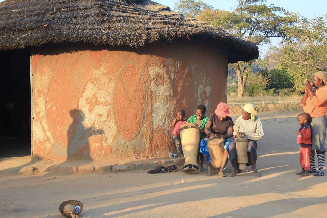 A painted Ndebele hut with drummers at golden hour