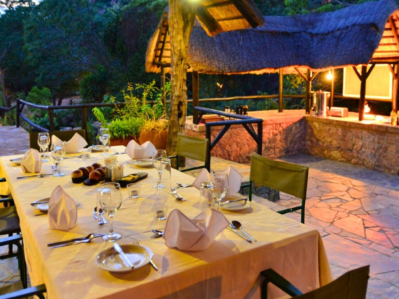 An outdoor dinner table set with white linen, wine glasses and lanterns at dusk
