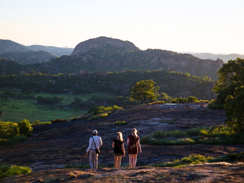 Three guests walking across a granite dome at golden hour with a guide