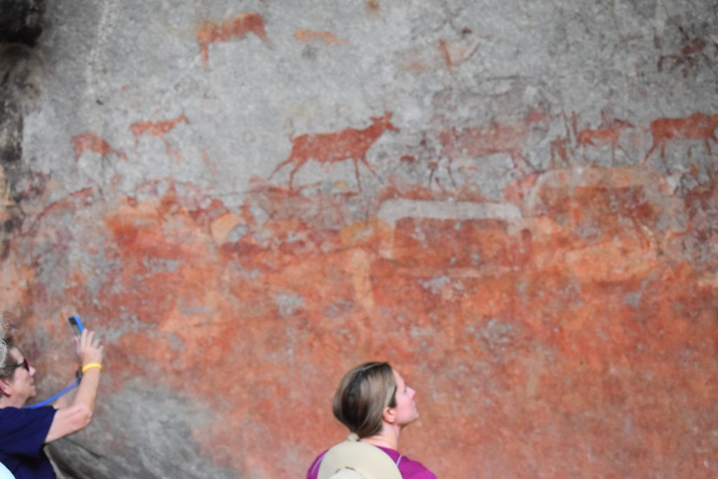 Two visitors looking up at antelope painted in red ochre on a granite wall