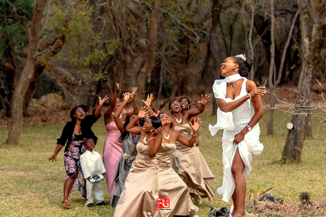 Bride and wedding party laughing during the bouquet moment among Matobo trees.