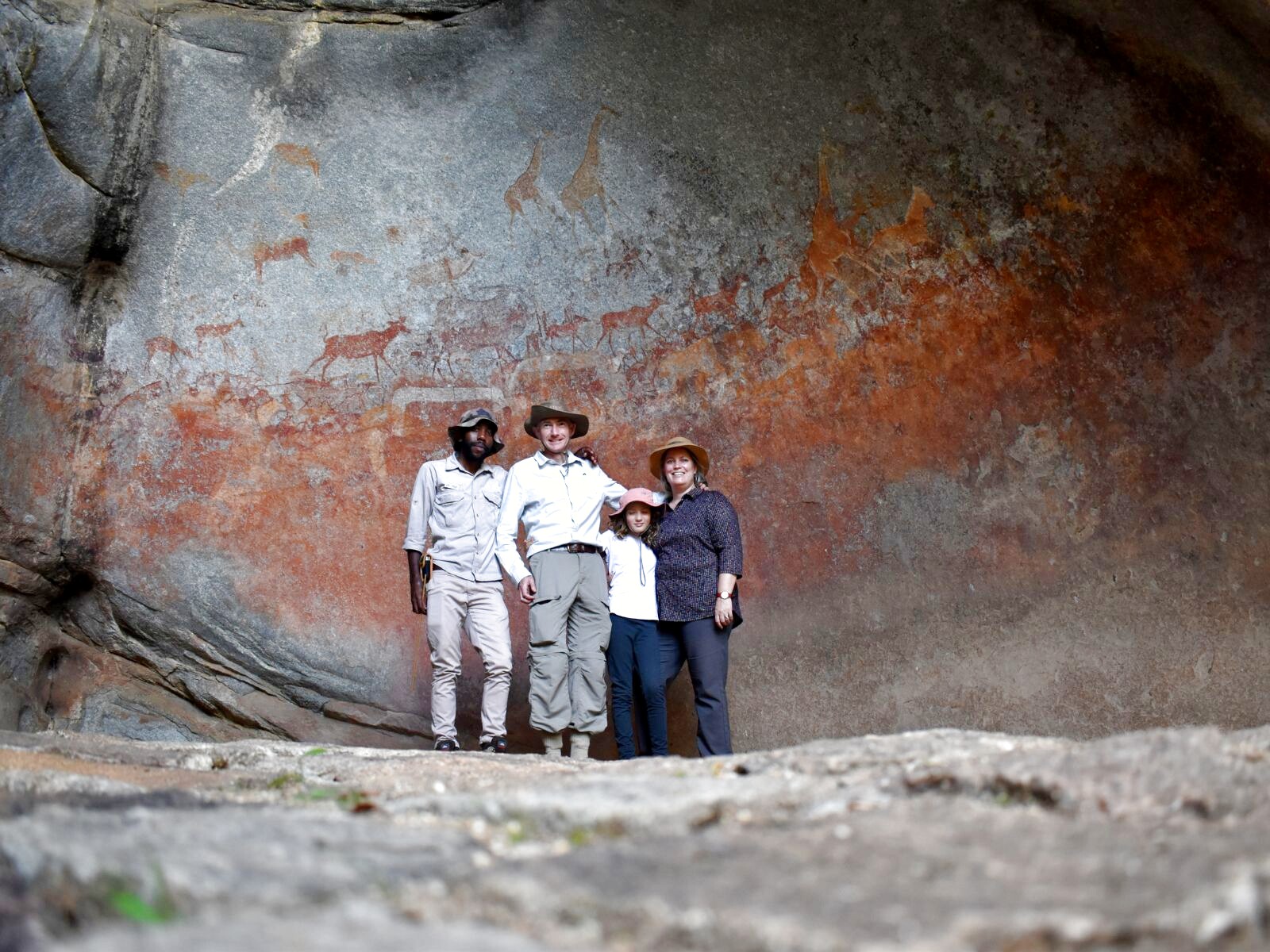 A family standing beneath a painted frieze of animals inside a granite cave